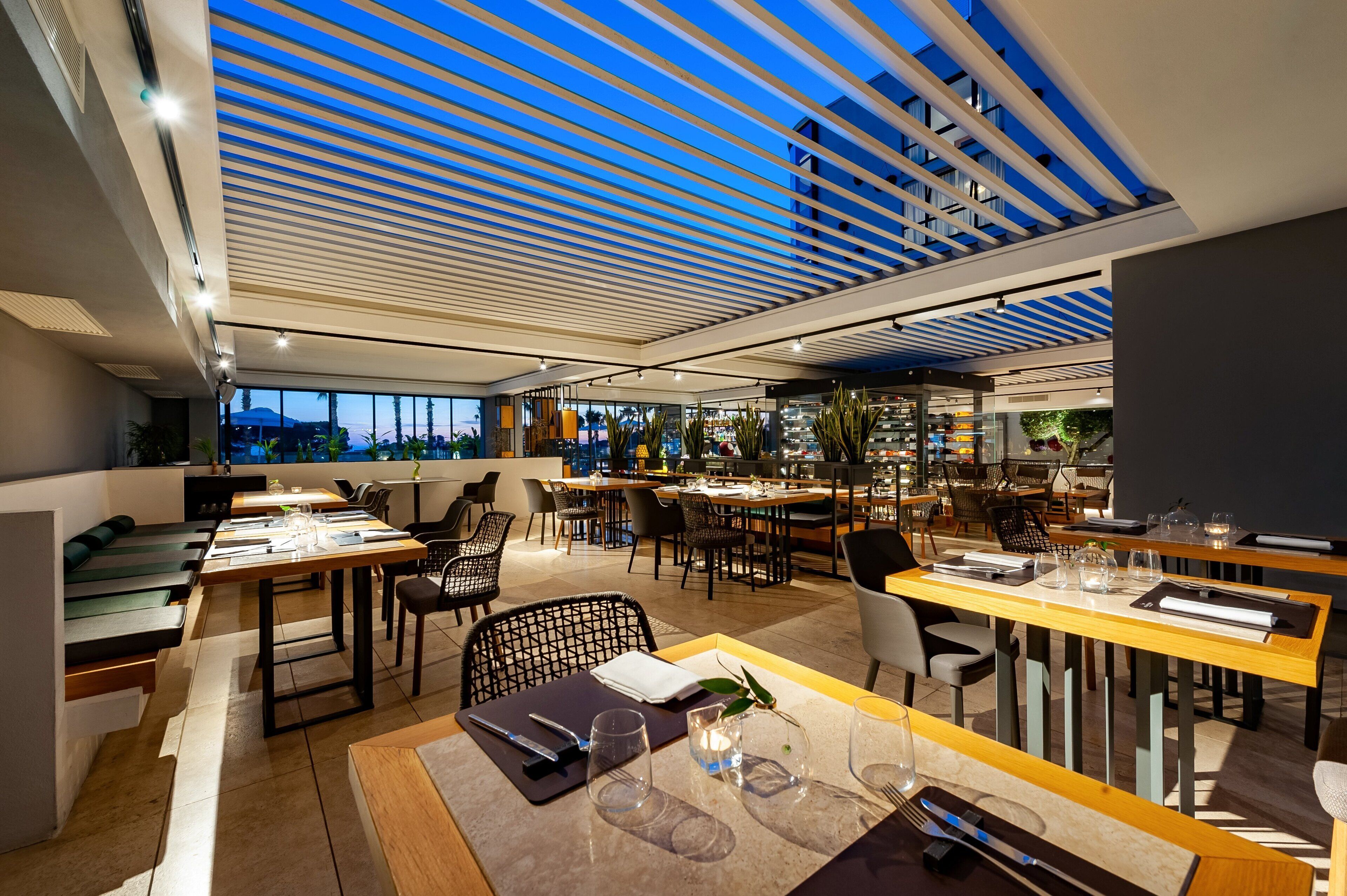 A modern restaurant with a high ceiling, large windows, and a variety of seating arrangements including tables and chairs.