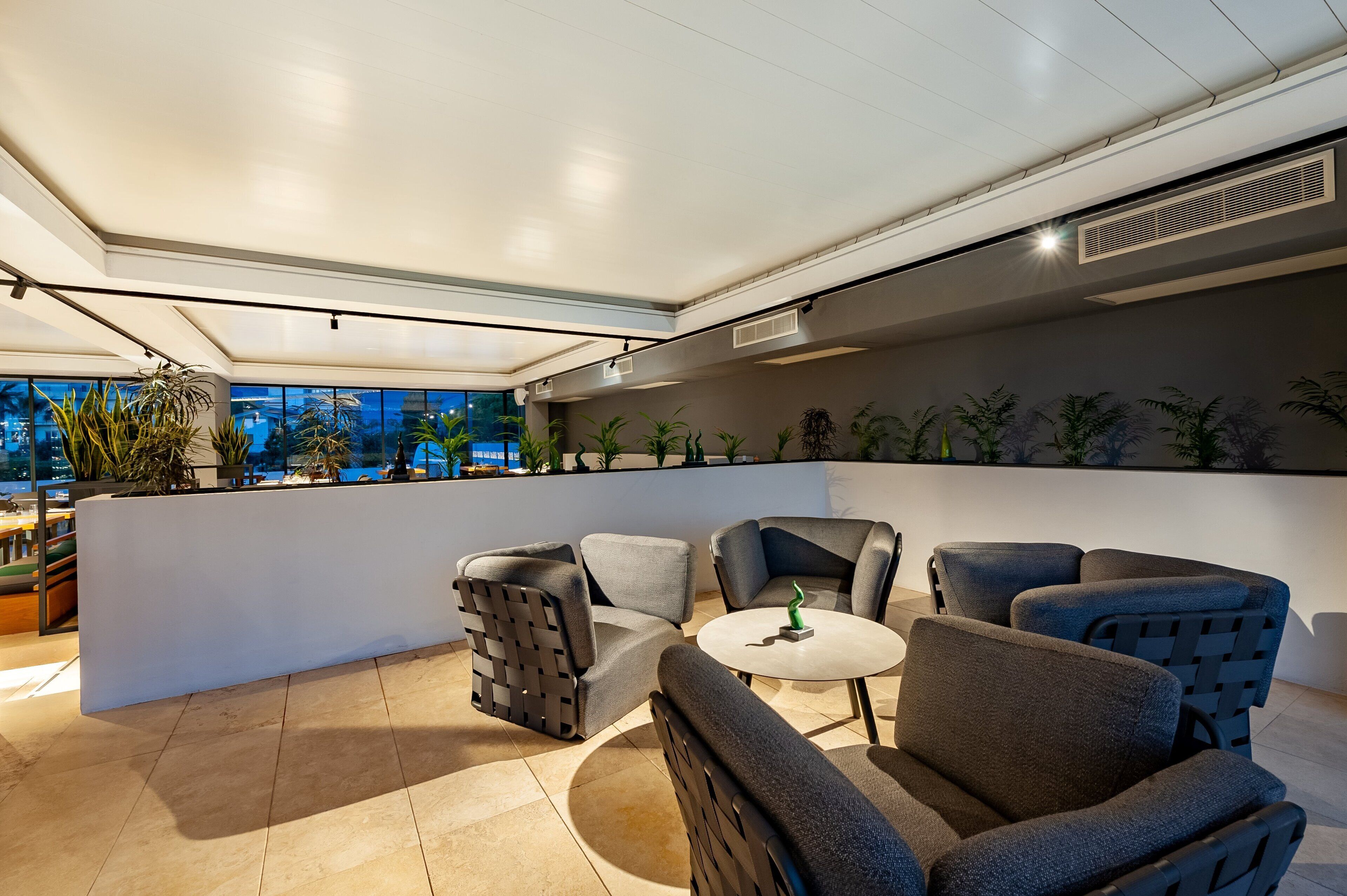 A modern lounge area with comfortable seating, a small table, and a view of the cityscape through large windows.