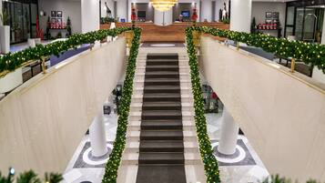 Vestíbulo de hotel con una escalera central, decorado con guirnaldas navideñas, y una lámpara de araña moderna y grande.