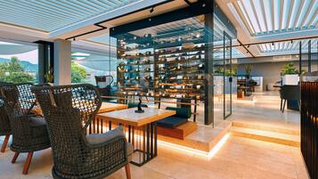 Ein modernes Interieur mit Korbstühlen, einem Holztisch und einer Glasvitrine für Weinflaschen.
