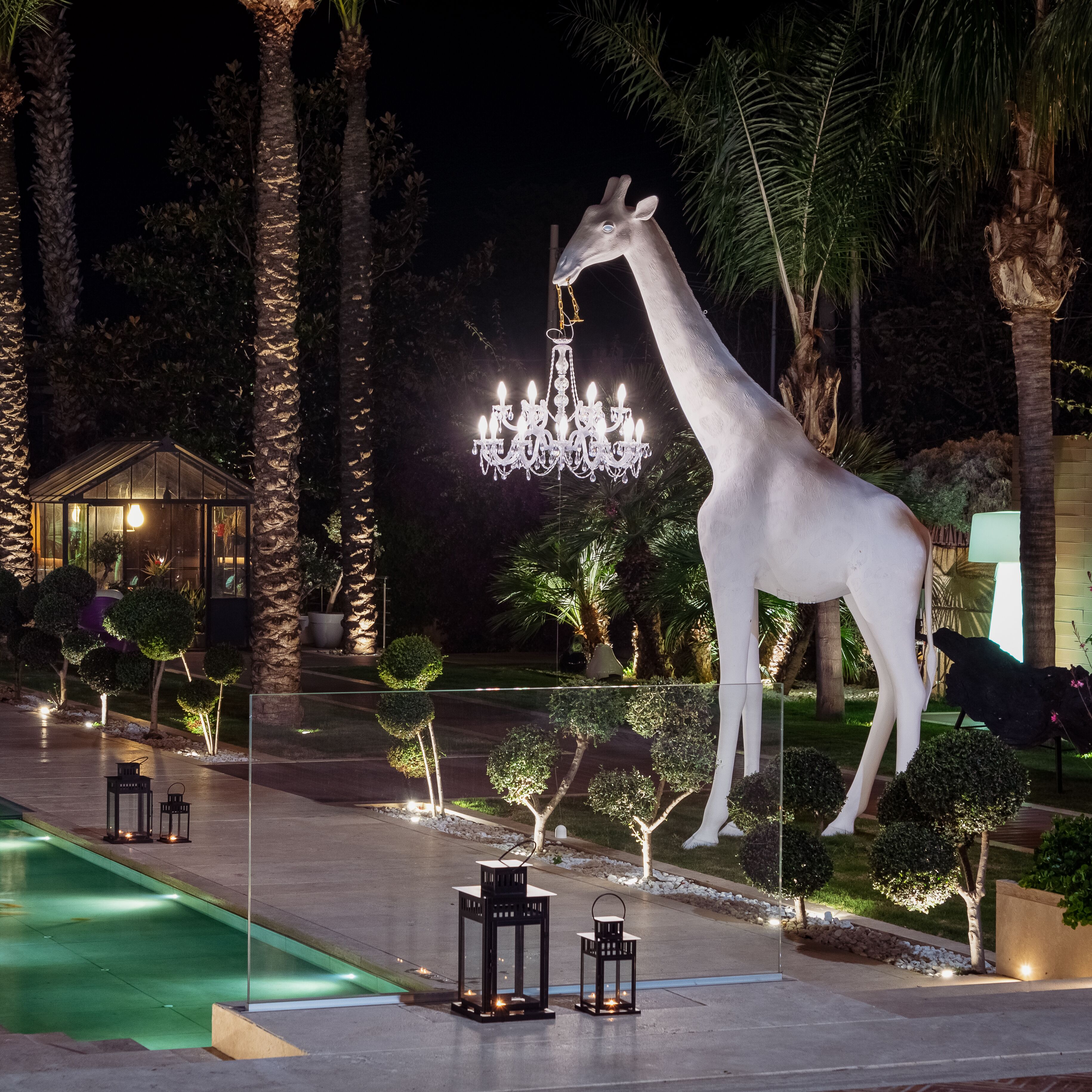 Eine große Giraffenskulptur mit einer Kronleuchter, umgeben von Palmen und einem Pool.
