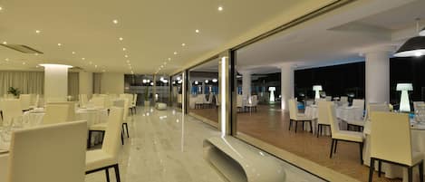 Un espace de restauration moderne avec des tables dressées pour le service, un banc incurvé et une vue dégagée grâce à de grandes portes vitrées.