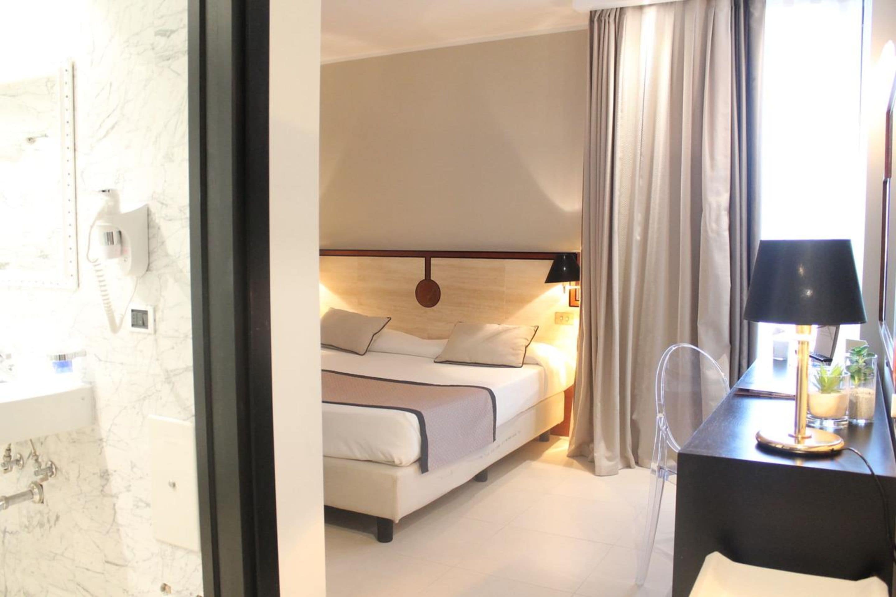 A hotel room with a bed, bedside lamp, and a desk with a lamp.