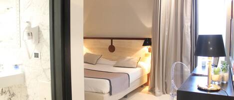 A hotel room with a bed, bedside lamp, and a desk with a lamp.