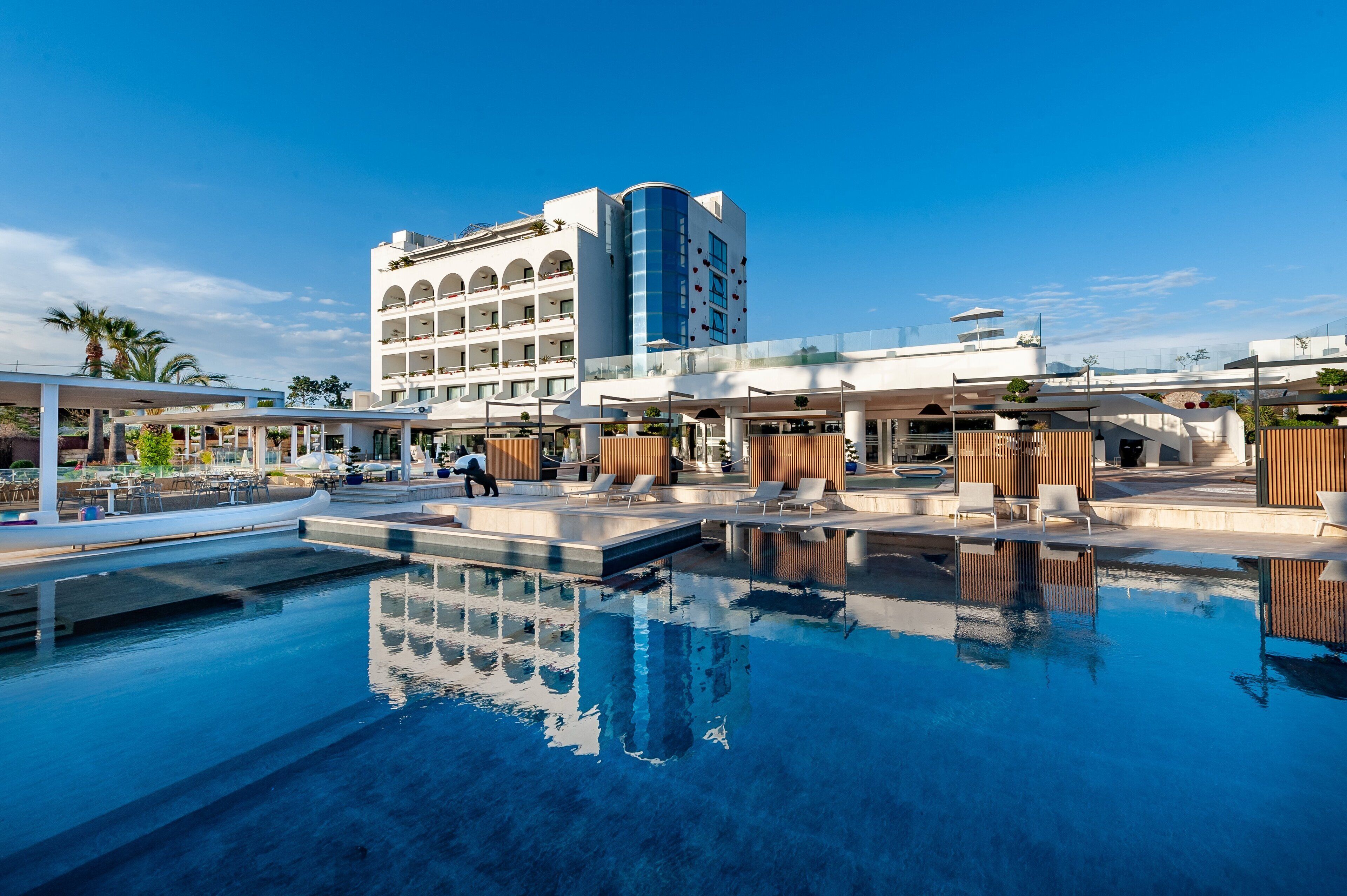 A hotel with a swimming pool, a multi-story building, and a covered outdoor area with seating.