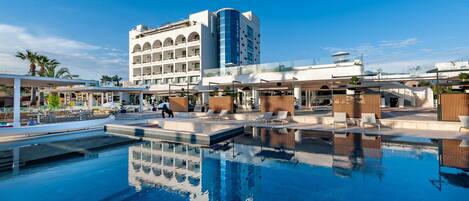 A hotel with a swimming pool, a multi-story building, and a covered outdoor area with seating.
