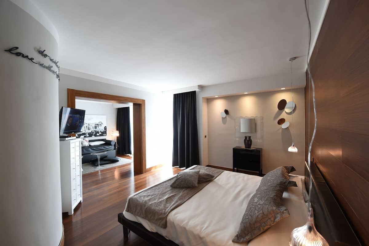 Un dormitorio moderno con cama, mesita de noche, lámpara y televisión en la habitación contigua.