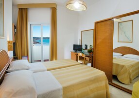 Habitación de hotel con dos camas, un escritorio con computadora, televisor y un espejo grande.