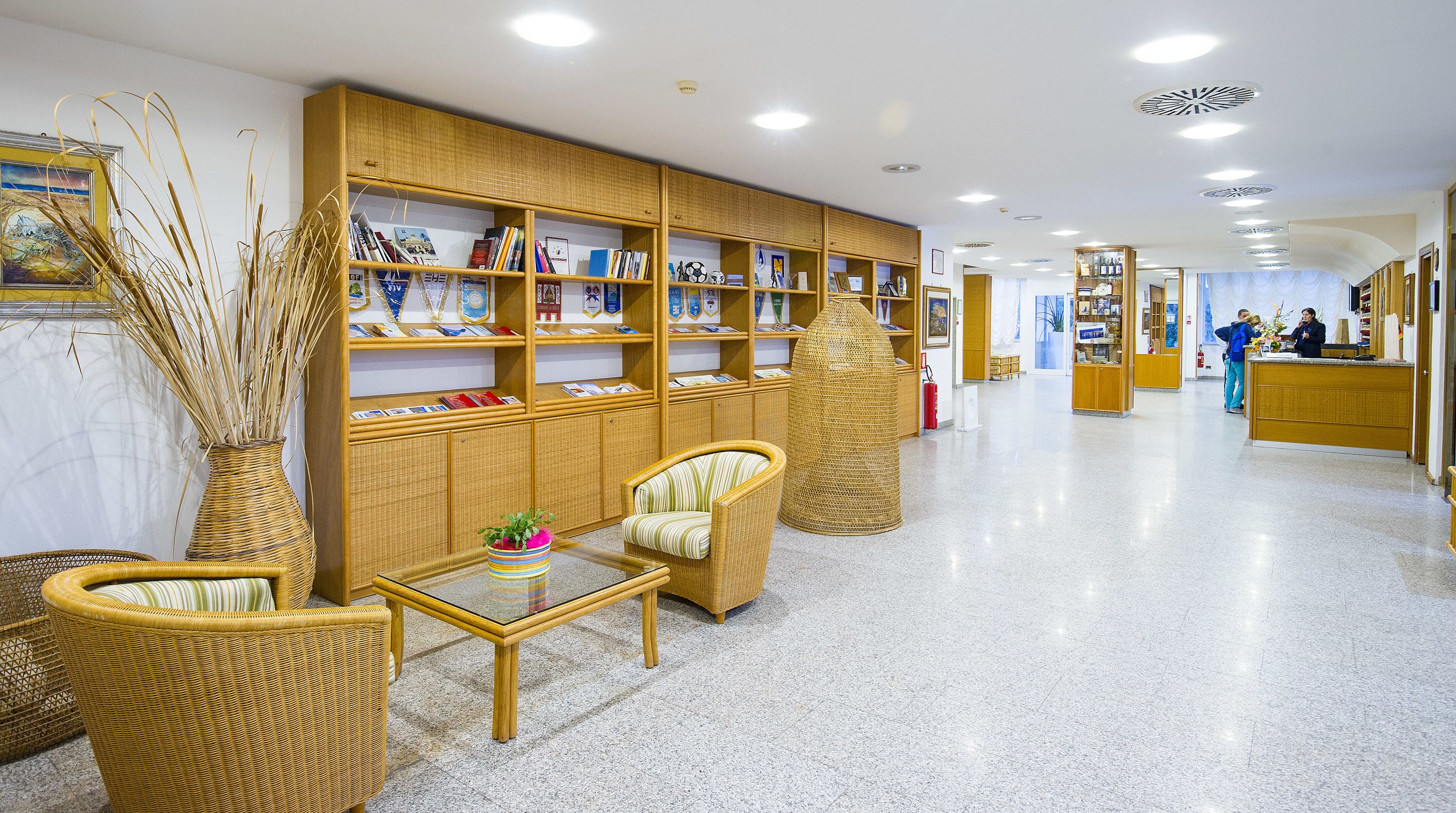 A spacious lobby with a polished tile floor, wicker furniture, and a large wooden bookshelf filled with books and decorative items.