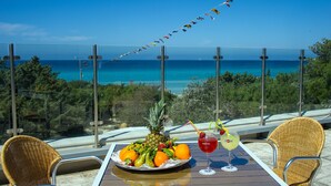 Una mesa con una bandeja de frutas y bebidas, con vista a una playa de aguas azules cristalinas y un faro a lo lejos.