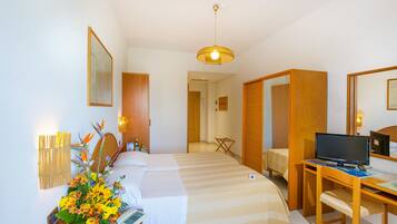 A hotel room with two beds, a desk with a computer, a small table, and a decorative plant.