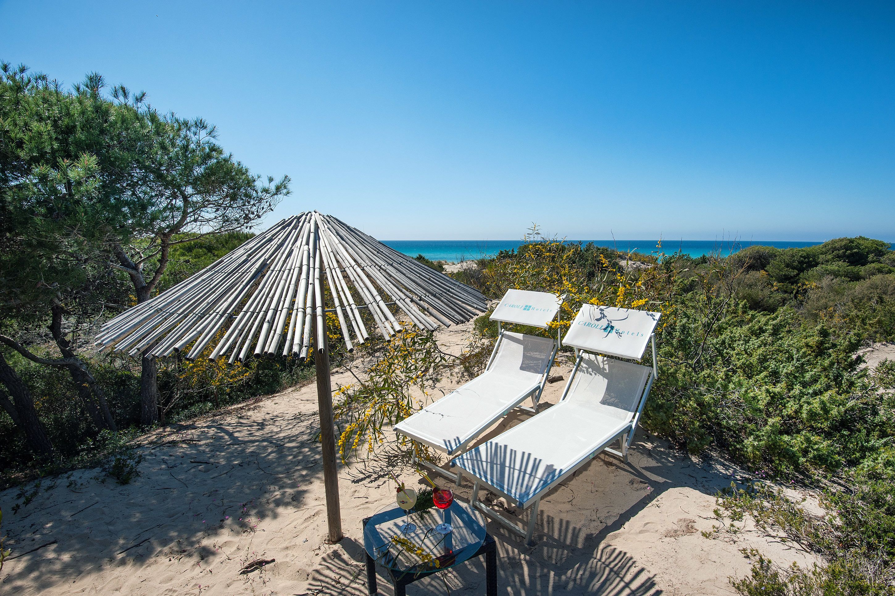 A beach with two lounge chairs and a bamboo umbrella.