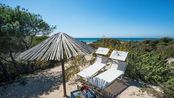A beach with two lounge chairs and a bamboo umbrella.