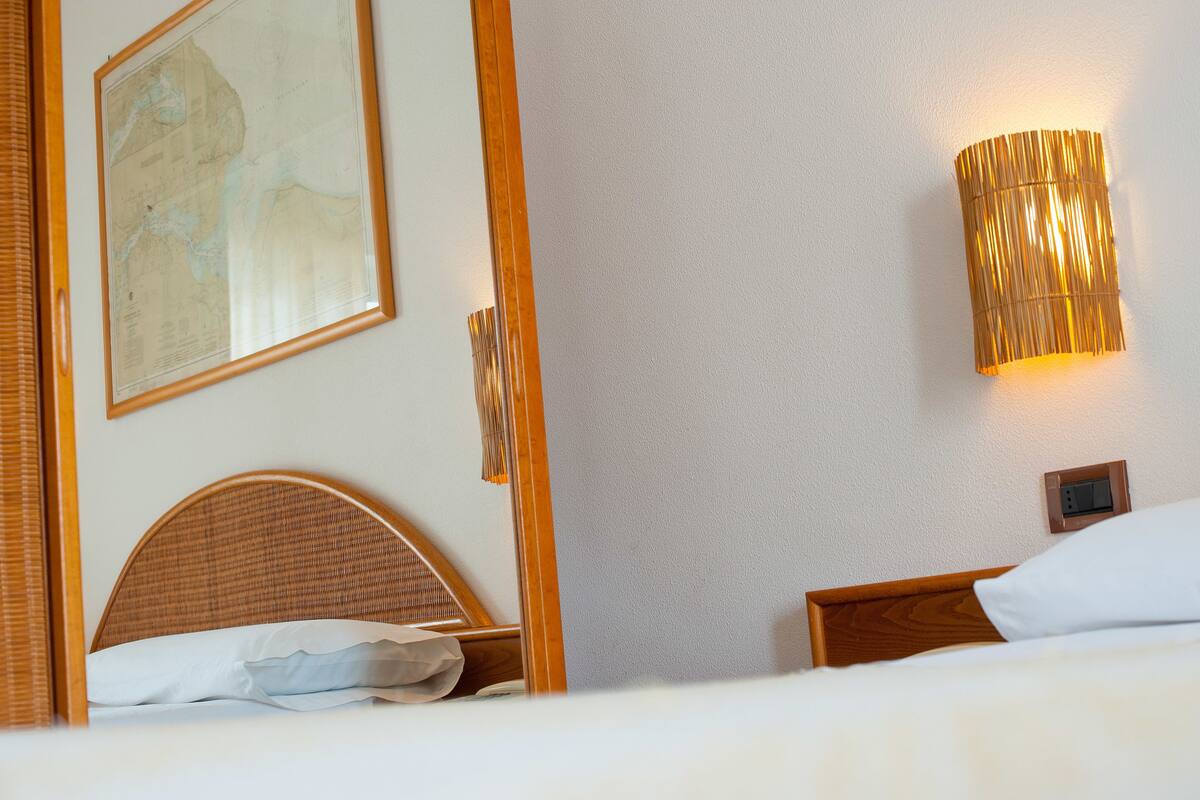A hotel room with a wooden headboard, a bed with white linens, a wall-mounted lamp, and a framed map on the wall.