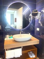 Un bagno con uno specchio rotondo, un lavandino bianco e un portascopevoli.