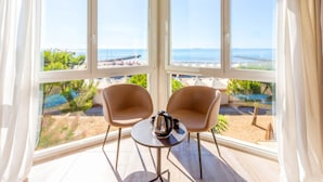 Una habitación soleada con dos sillas y una mesa, ventanas amplias con vista a una playa y al océano.