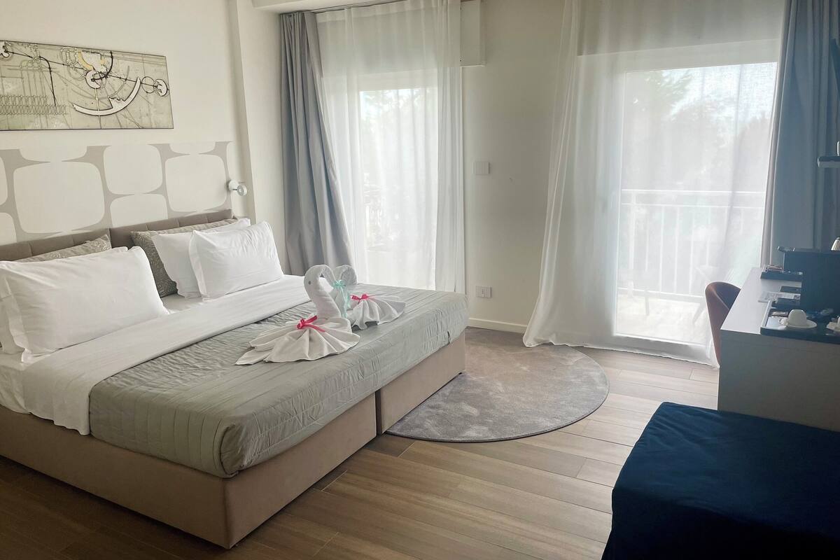 A hotel room with a bed, a desk, and a large window with curtains.
