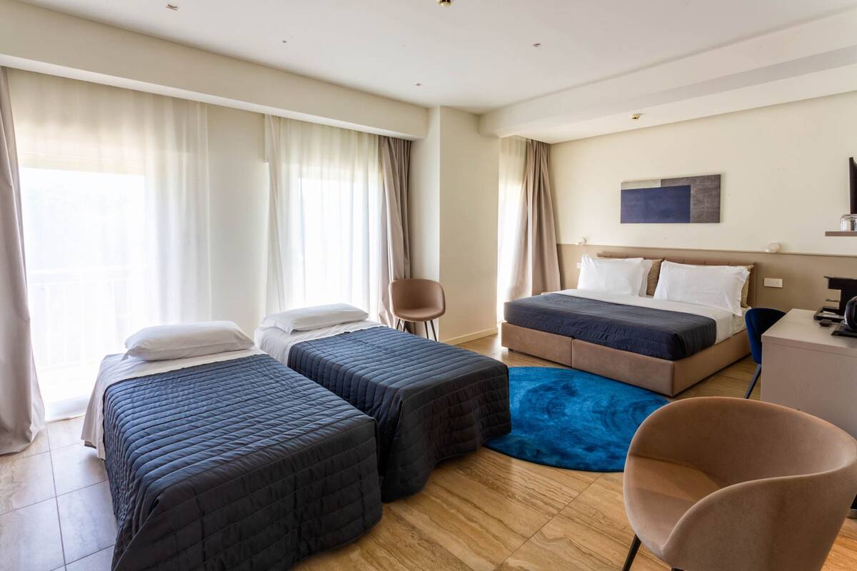 A hotel room with two beds, a desk, a chair, and a large window with curtains.