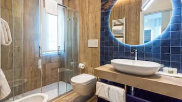 Un baño moderno con cabina de ducha de vidrio, inodoro, lavabo con espejo grande y pared de azulejos azules.