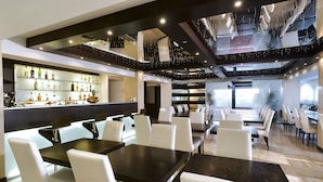 Un restaurante moderno con una zona de bar, varias mesas para comer y un alto techo con vigas a la vista.