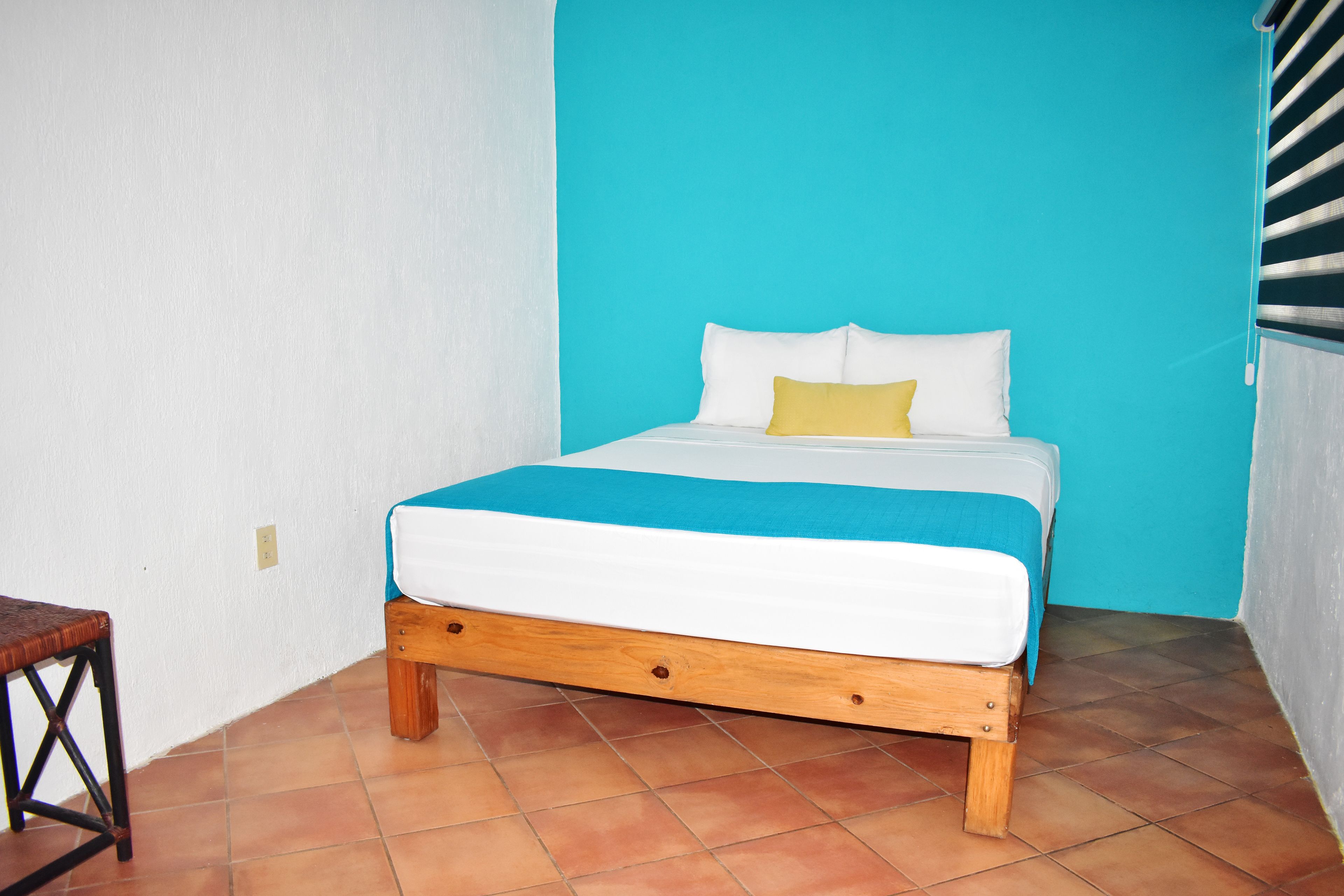 Una cama con estructura de madera, ropa de cama blanca y azul, y una almohada amarilla.