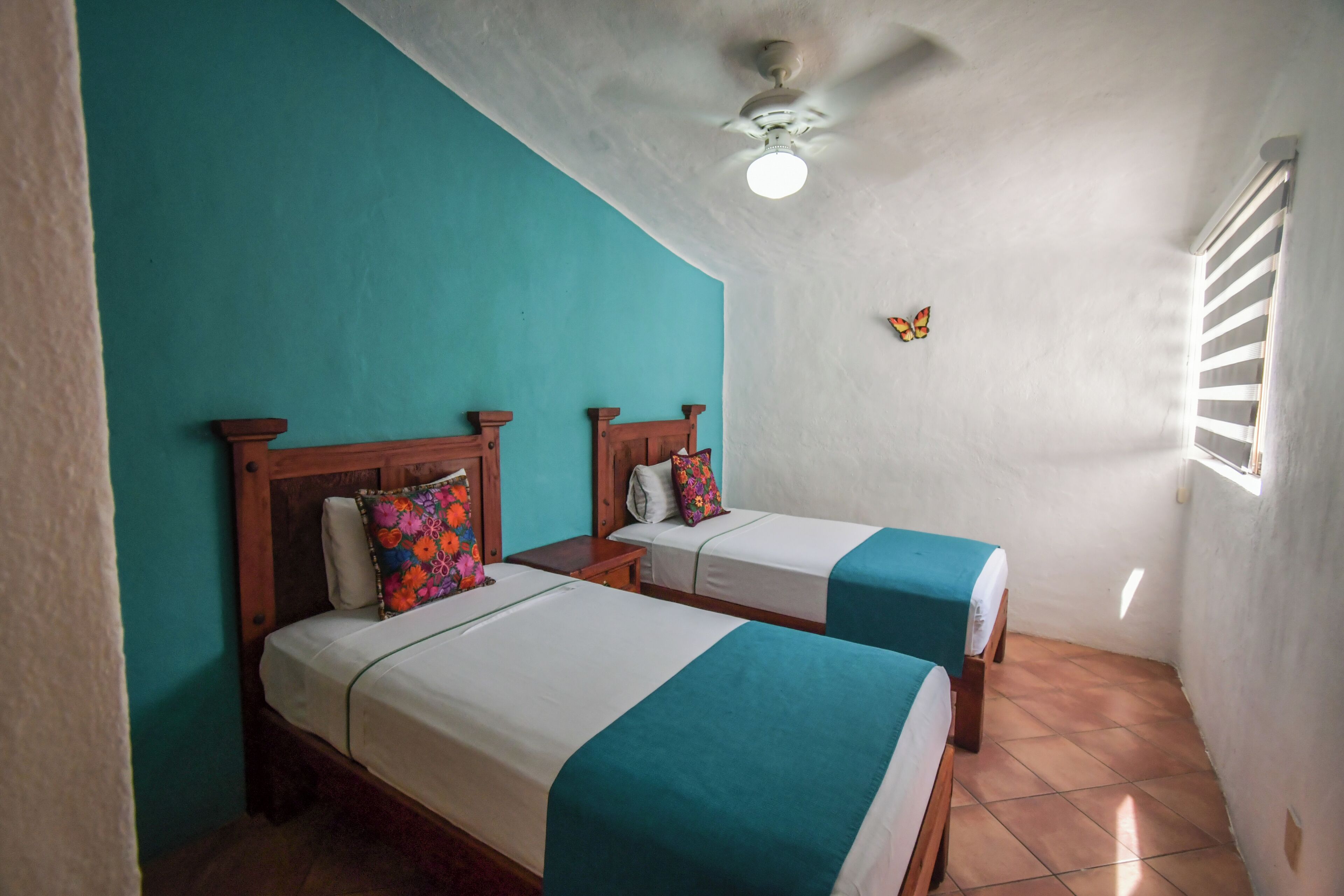 Two single beds with wooden headboards and teal bedspreads in a room with white walls and a sloped ceiling.