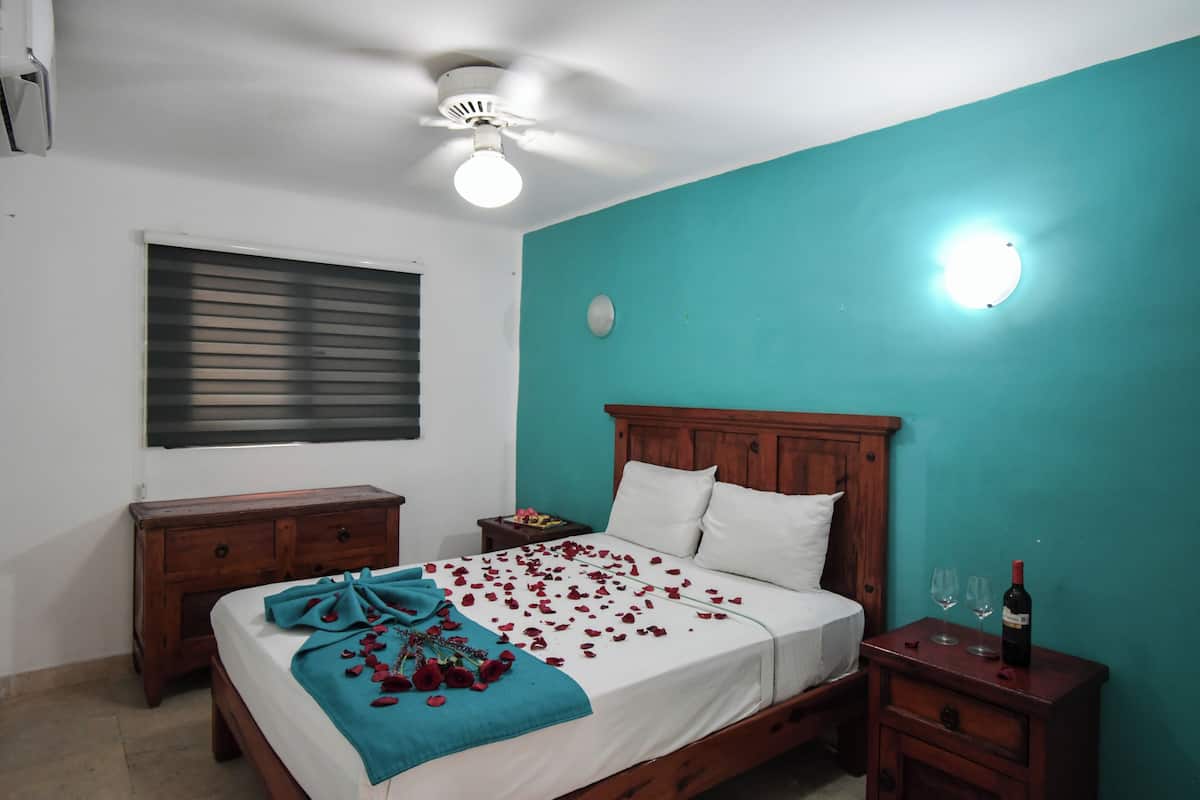 A bedroom with a bed, wooden headboard, bedside tables, a ceiling fan, and a wall-mounted light.