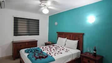 Une chambre à coucher comprenant un lit, une tête de lit en bois, des tables de chevet, un ventilateur de plafond et une lampe fixée au mur.