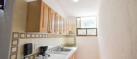 A compact kitchen with wooden cabinets, a tiled backsplash, a coffee maker, and a window providing natural light.