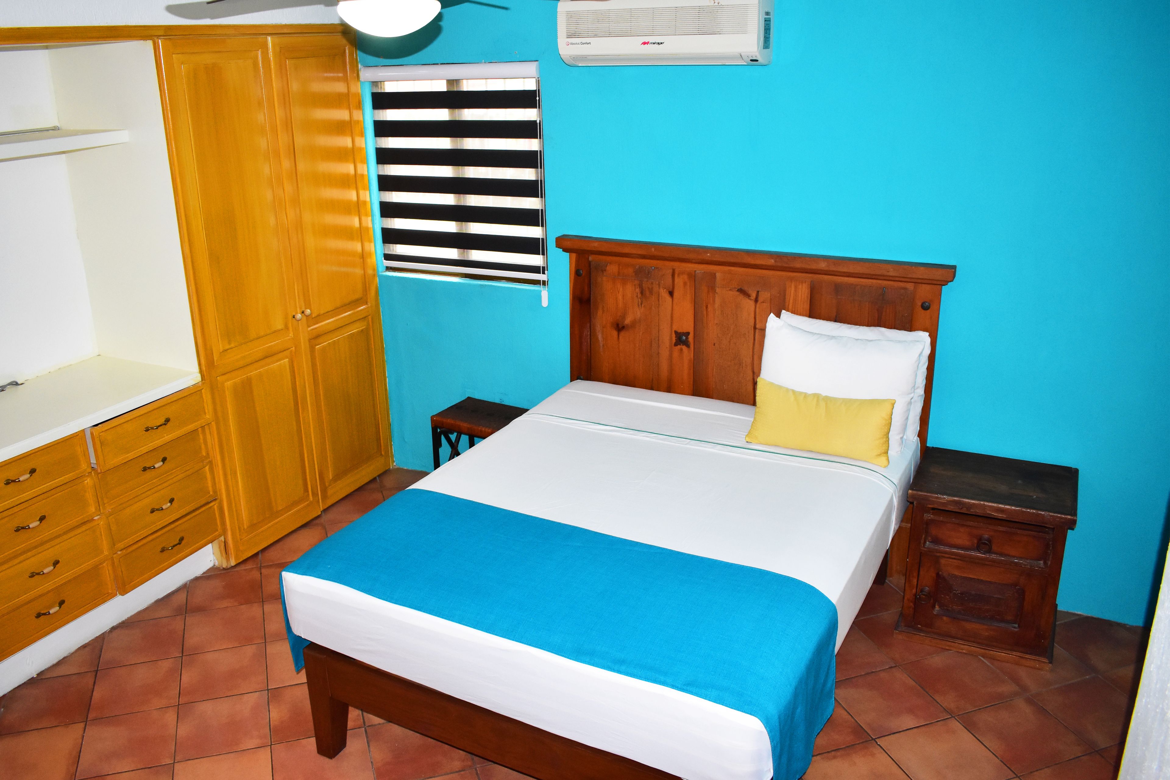 A bedroom with a bed, wooden wardrobe, bedside tables, and a window with blinds.