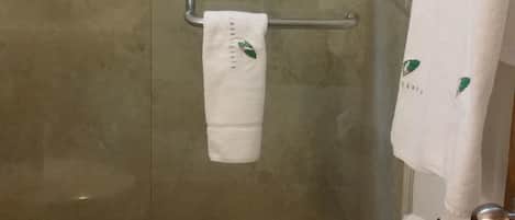Un baño con cabina de ducha de vidrio, inodoro, toallero con toalla y un cubo de basura.