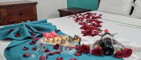 Una cama impecable adornada con pétalos de rosa, una botella de vino y una bandeja de bombones.