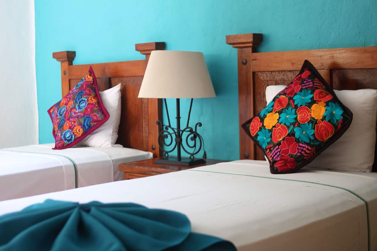 A hotel room with two beds, each with a wooden headboard, a bedside lamp, and colorful floral pillows.