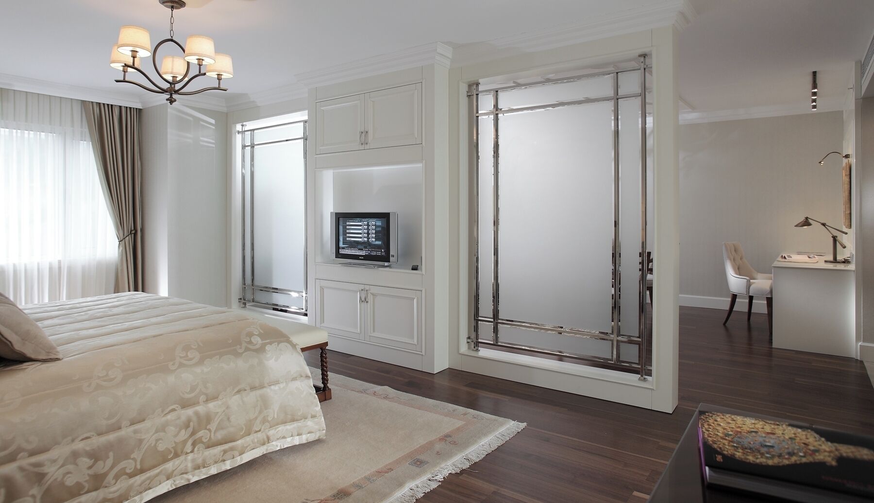 A bedroom with a bed, a TV, a desk with a chair, and a wardrobe.