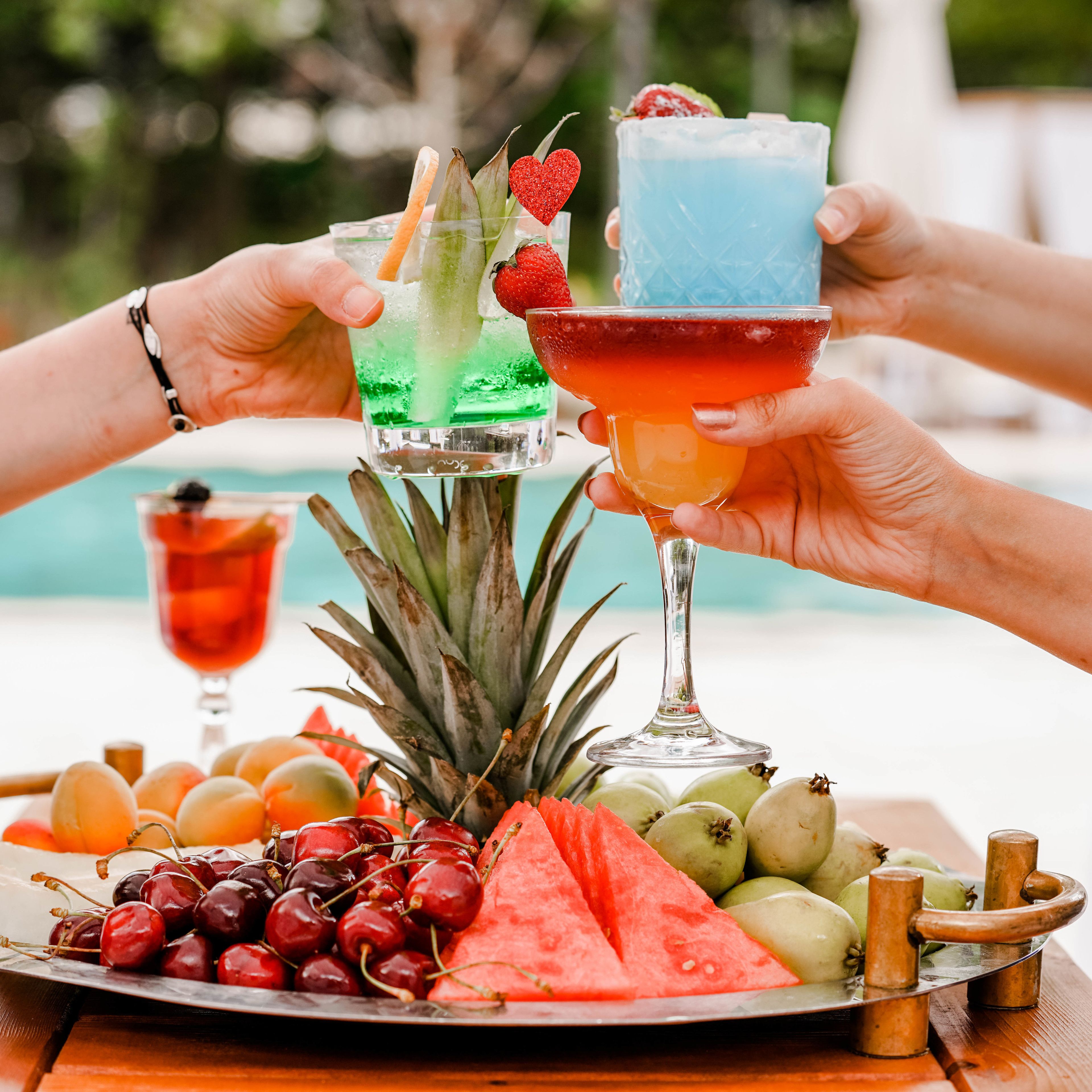 Escena tropical con piscina, una bandeja de frutas y dos cócteles.