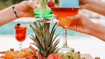 Escena tropical con piscina, una bandeja de frutas y dos cócteles.