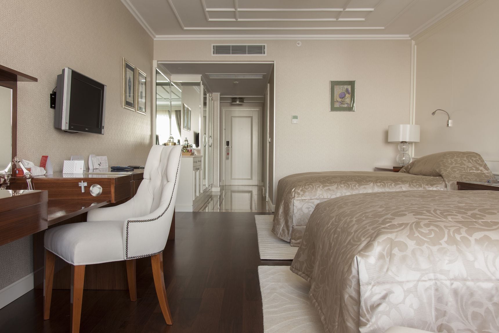 Une chambre d’hôtel équipée d’un bureau, d’une chaise, de deux lits, d’une télévision et d’une salle de bain visible à travers une porte ouverte.