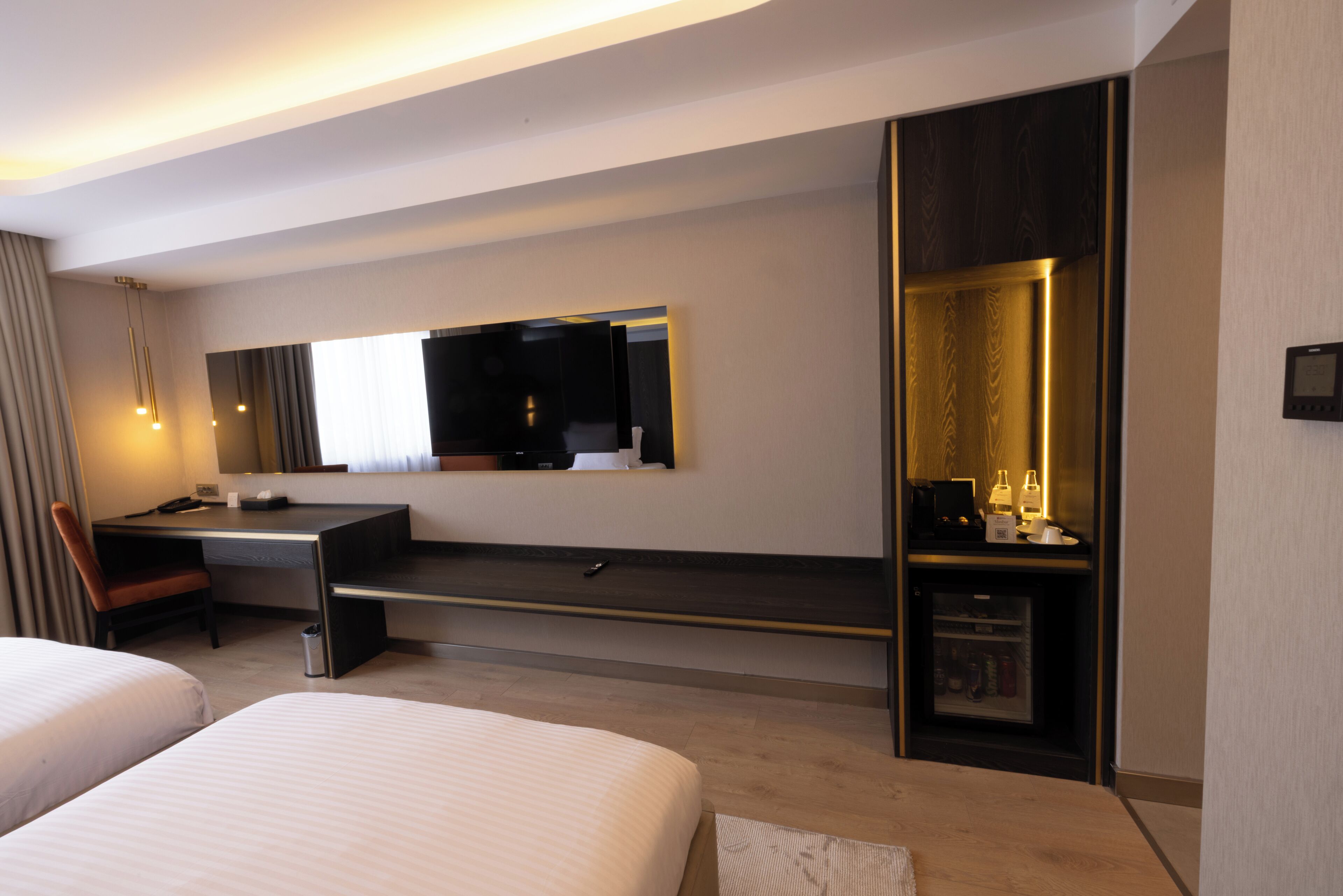 Una habitación de hotel moderna con una cama grande, un escritorio, una silla, un televisor y un mini bar.