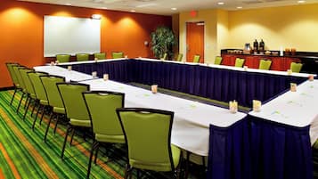 A conference room with a long table, green chairs, a projector screen, and a coffee station.
