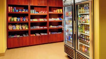 Un refrigerador con aperitivos y bebidas en el vestíbulo de un hotel, con varias estanterías llenas de diferentes opciones.