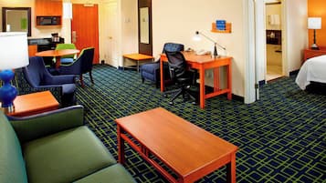 A hotel room with a sofa, a desk, a chair, a small table, a lamp, a microwave, a mirror, a closet, and a bed.