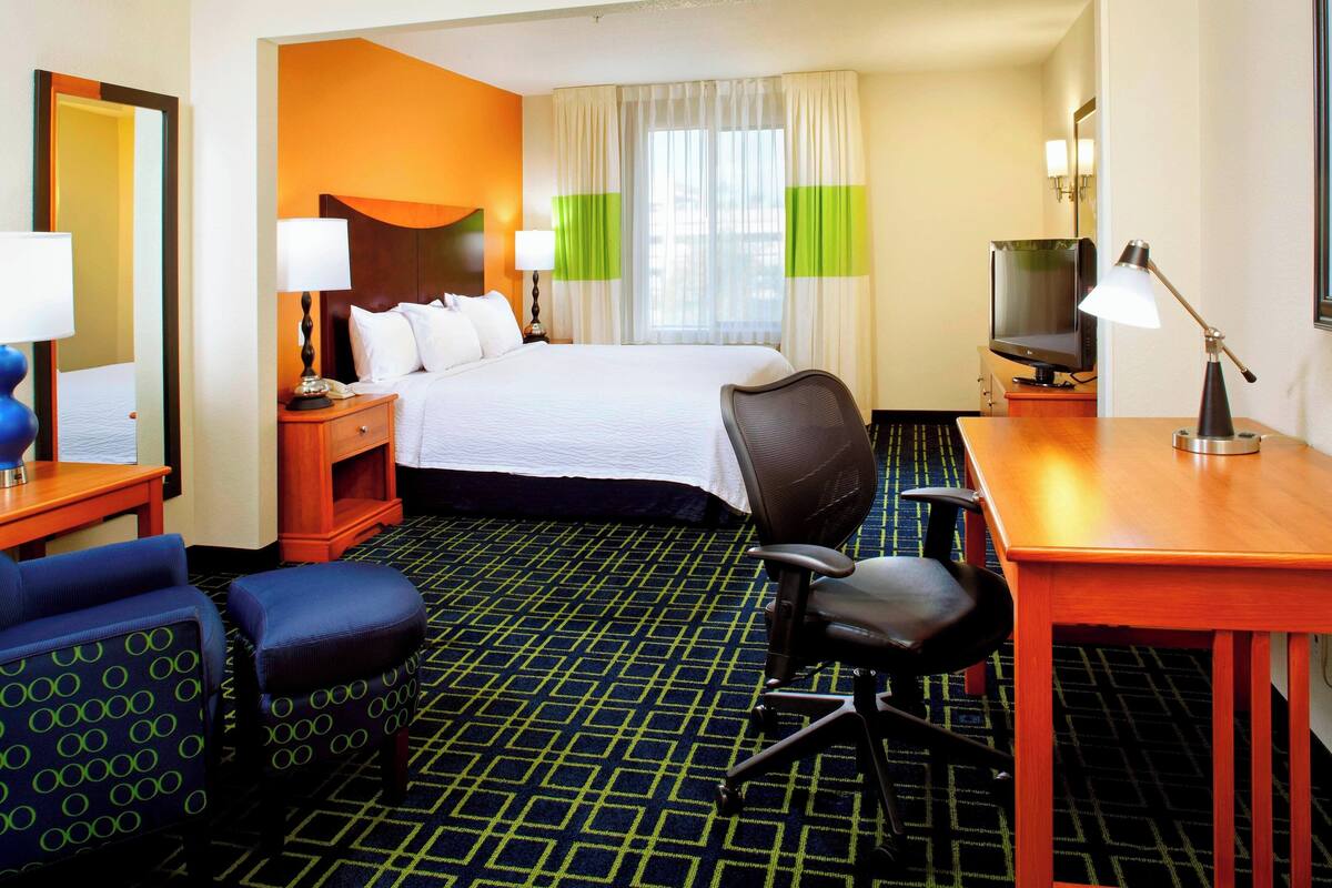 A hotel room with a bed, a desk, a chair, a TV, and a lamp.