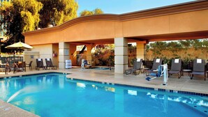 A swimming pool with lounge chairs and umbrellas, surrounded by a covered area with a curved roof. - Fairfield Inn & Suites by Marriott Phoenix Midtown (Phoenix)