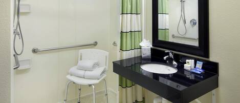 Un baño con ducha accesible para sillas de ruedas, un lavamanos con encimera negra y un espejo sobre el lavamanos.