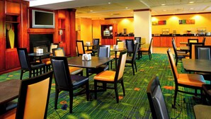 A hotel lobby with multiple dining tables and chairs, a television mounted on the wall, and a counter with various amenities. - Fairfield Inn & Suites by Marriott Phoenix Midtown (Phoenix)