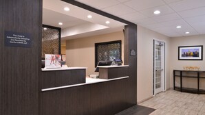 A hotel reception area with a dark wood reception desk, a laptop, and a framed cityscape picture on the wall. - Candlewood Suites Austin-Round Rock by IHG (Round Rock)