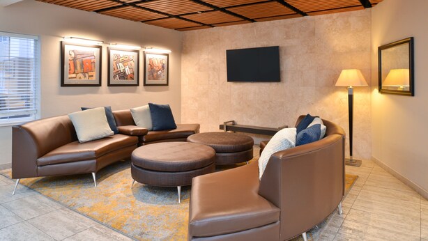 A modern living room with a sectional sofa, ottomans, and a flat-screen TV mounted on the wall. - Candlewood Suites Austin-Round Rock by IHG (Round Rock)