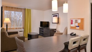A hotel room with a round dining table, two chairs, a sofa, a TV, a lamp, and a bulletin board. - Candlewood Suites Austin-Round Rock by IHG (Round Rock)