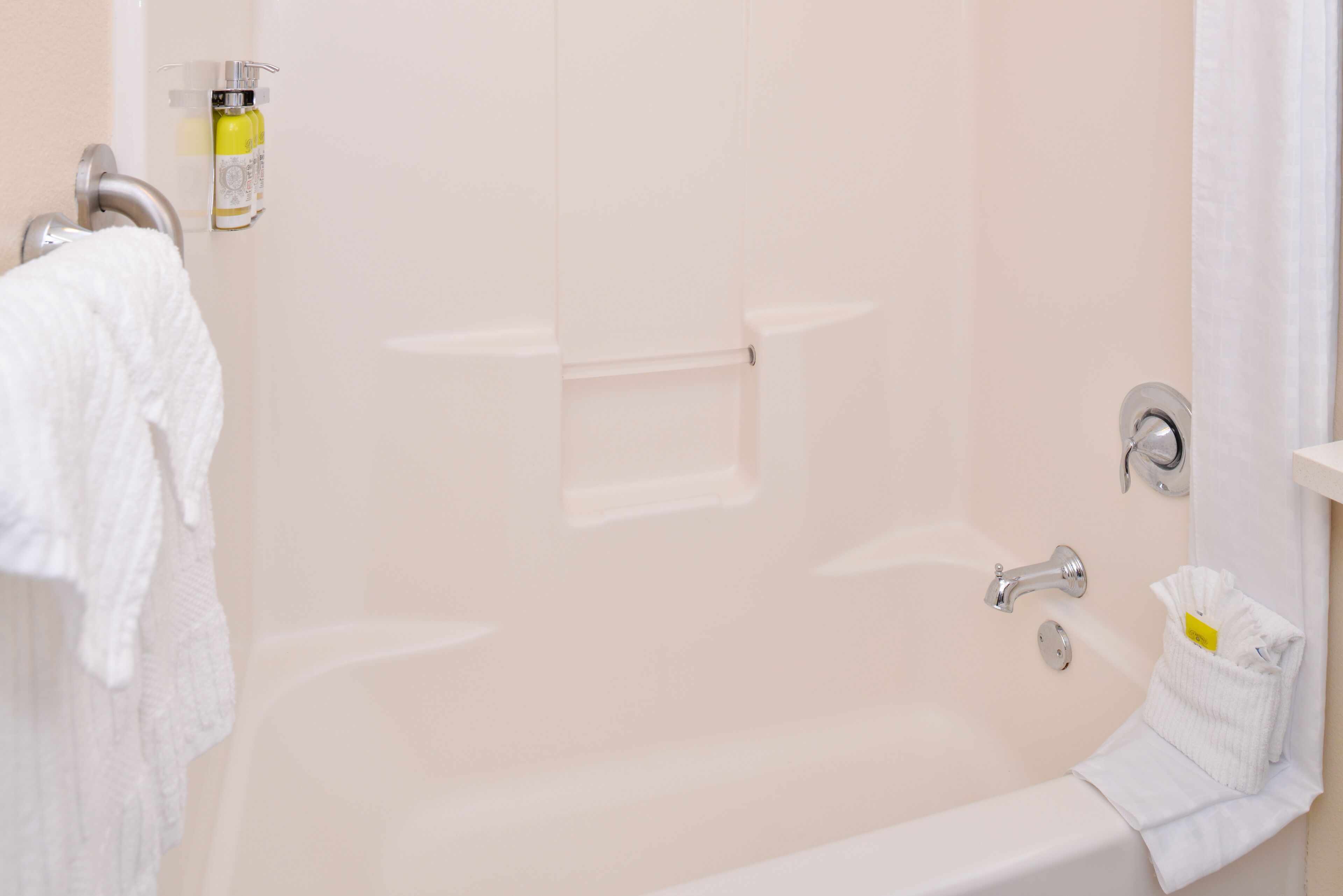 A bathtub with a handheld showerhead, a bottle of shampoo, and a towel rack.