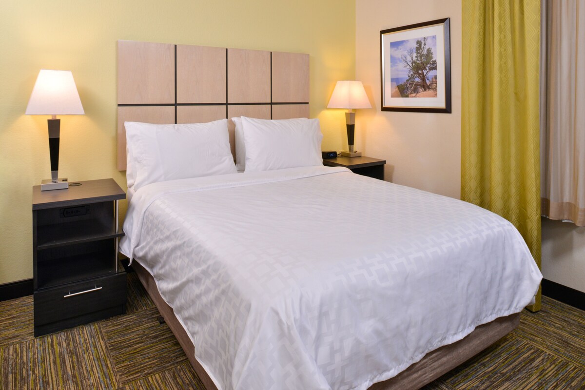 A neatly made bed with white linens, a wooden headboard, two bedside tables with lamps, and a framed picture on the wall.